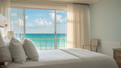 Sunlit coastal bedroom overlooking turquoise ocean, bed facing sliding balcony doors