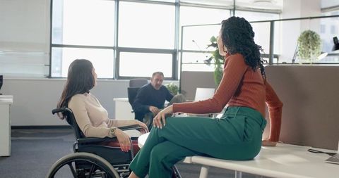 Diverse team collaborating around round table with wheelchair in modern open-plan office