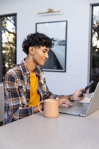 Young Man Working from Home Using Laptop and Smartphone in Cozy Kitchen