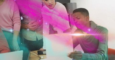Team collaborating and reviewing documents around laptop in modern creative workspace