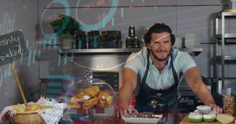 Smiling Male Baker Leaning Over Counter with Fresh Pastries, Cupcakes, Rustic Bakery