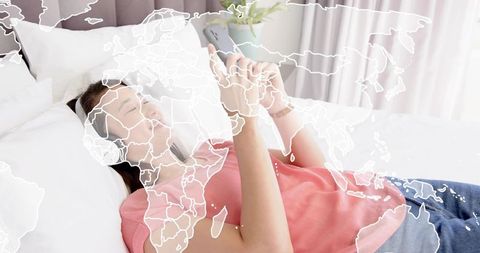 Relaxing asian woman lying on bed using smartphone and headphones, global map overlay