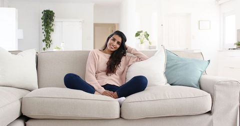 Smiling Indian Woman Relaxing on Modern Light Gray Sofa in Tranquil Living Room
