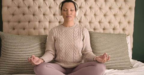Woman Meditating on Bed with Headphones in Cozy Environment