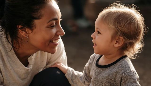 Smiling caregiver leaning toward toddler in warm sunlit moment of gentle connection