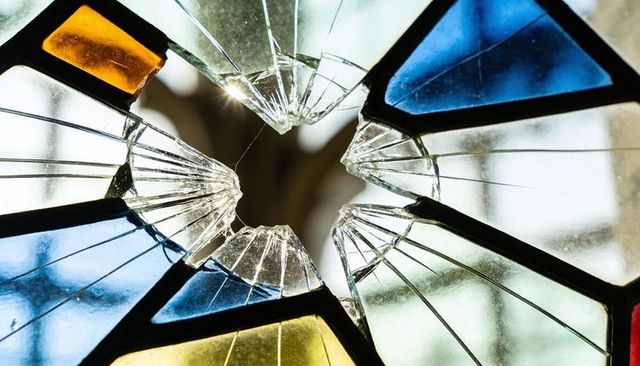 Sunlight revealing shattered stained glass panel with central hole, blue and yellow panes