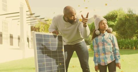 Man explaining solar energy while holding solar panel and pointing in sunlit backyard with girl