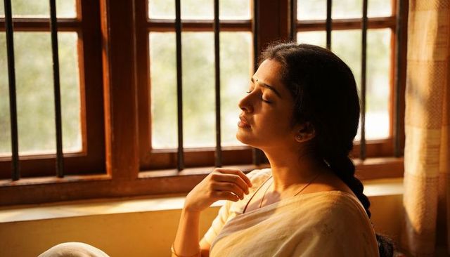 Indian woman resting by sunlit window in sari, peaceful contemplative portrait