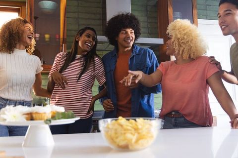 Diverse friends laughing and chatting around kitchen island with snacks and cupcakes