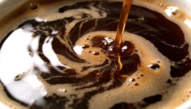 Pouring dark coffee creating swirling crema vortex with glossy bubbles macro close-up