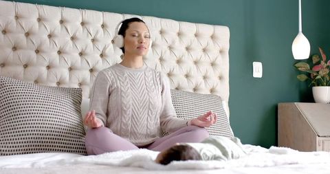 Asian Mother Meditating on Bed with Sleeping Infant