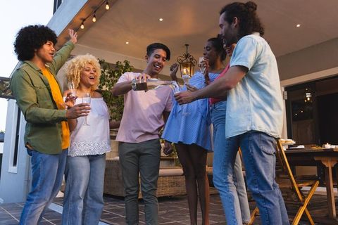 Multicultural friends celebrating on patio at twilight pouring champagne and toasting
