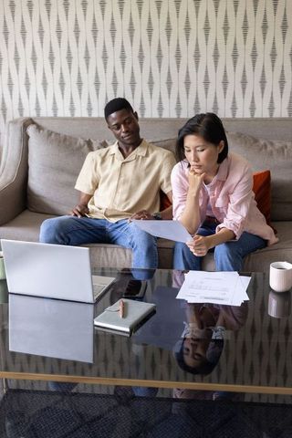 Couple reviewing finances on sofa with laptop and documents for budget planning