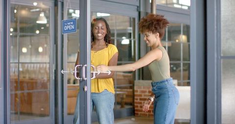 Two african american women opening cafe door smiling friendship casual urban lifestyle