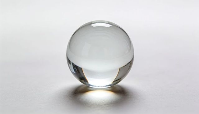 Crystal glass sphere reflecting light and casting soft shadow on minimal white surface