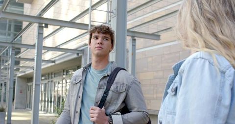Two students standing under metal canopy at modern campus entrance wearing denim jackets