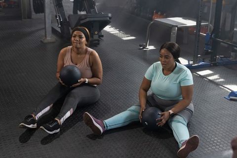 African american women working out with medicine balls doing seated russian twists in gym
