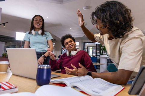 Multiracial Adults Collaborating and Studying with Laptop and Textbooks in Coworking Space
