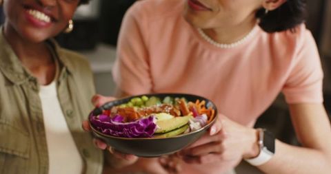 Friends sharing vibrant plant-based bowl with avocado, purple cabbage, edamame