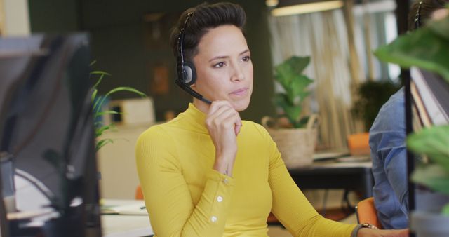 Customer service representative wearing a headset focused on providing assistance from modern office workspace. Ideal for illustrating concepts related to customer support, helplines, call centers, and professional work environments.