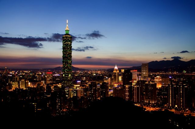 Panoramic view of Taipei City at dusk featuring Taipei 101 skyscraper lit up against a transitioning sky from evening to night. Ideal for use in travel advertisements, promotional content for Taiwan, architectural features, urban photography, and illustrating vibrant city life.