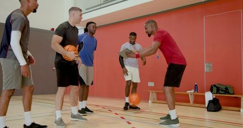 Coach reviewing game plan with diverse male basketball team on indoor hardwood court