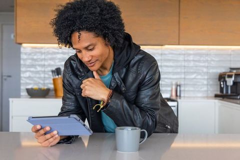 African american man leaning on kitchen island browsing tablet with coffee mug