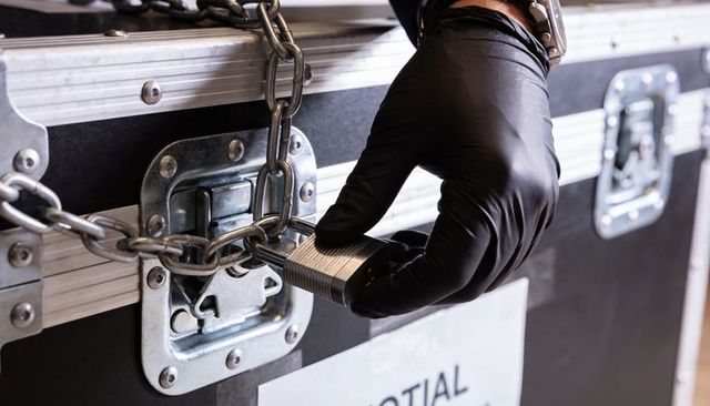 Gloved hand locking heavy-duty padlock on flight case chain for equipment security