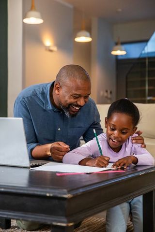 African american father helping daughter with homework at coffee table, studying together