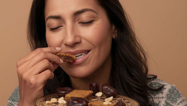 Smiling woman savoring date and nut energy bar closeup, warm tones