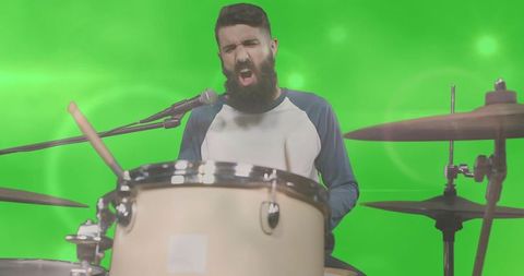 Bearded drummer singing and playing drum kit on green screen studio background