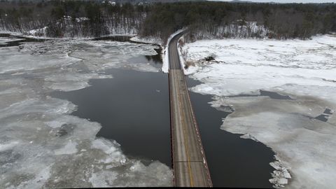 Long narrow bridge crossing partially frozen river, winter road stretching through marsh
