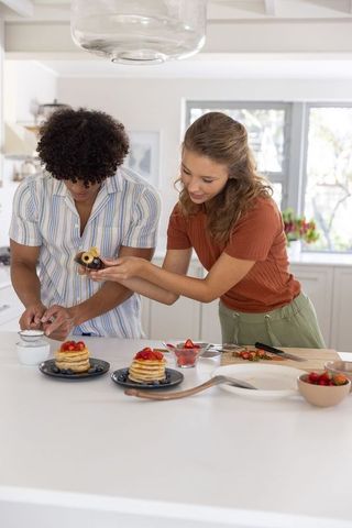 Young couple preparing pancake stacks with strawberries in bright modern kitchen