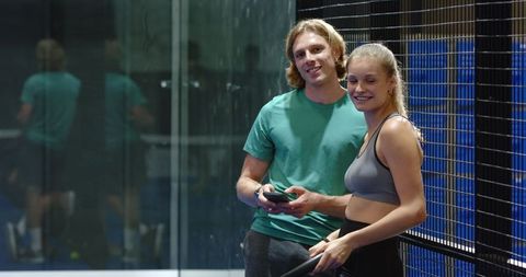 Couple Relaxing on Padel Court Holding Smartphone and Racket