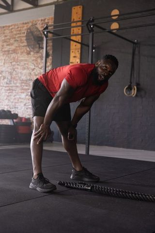 African american athlete bending and breathing heavily after battle rope workout in gym