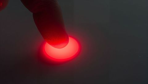Fingertip pressing glowing red button on dark touch panel close-up macro technology control interfac