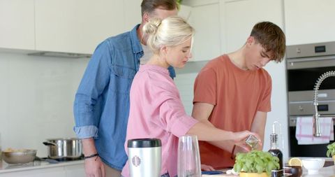 Family cooking together in bright modern kitchen with teen preparing meal and herbs