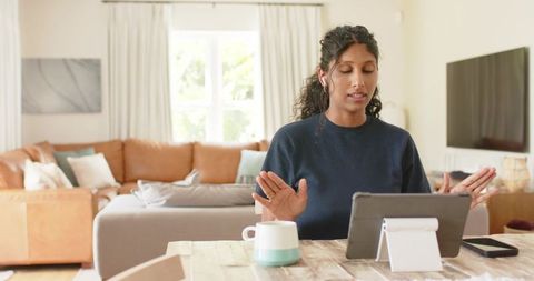 Indian woman working remotely on tablet in cozy living room with mug and smartphone