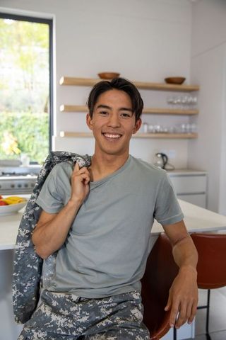 Asian male smiling and holding camo jacket while leaning on modern kitchen island