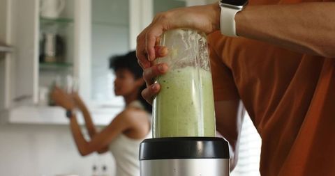 Couple blending green smoothie in bright modern kitchen for healthy morning routine