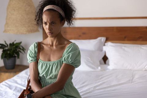 African american woman sitting on bed looking contemplative wearing puff-sleeve dress and smartwatch