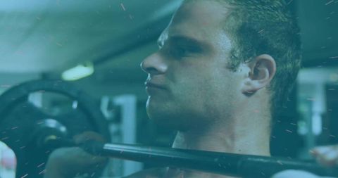 Muscular man balancing barbell indoors