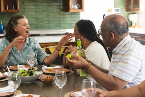 Friends chatting, passing wine and sharing salad around dining table during cozy home dinner