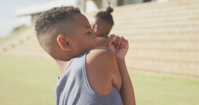 Image of focused african american boys stretching outdoors on sunny day. primary school education, sport and exercising.