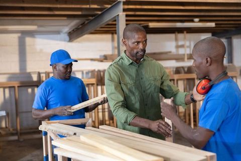 African american foreman supervising woodworkers inspecting lumber in rustic workshop