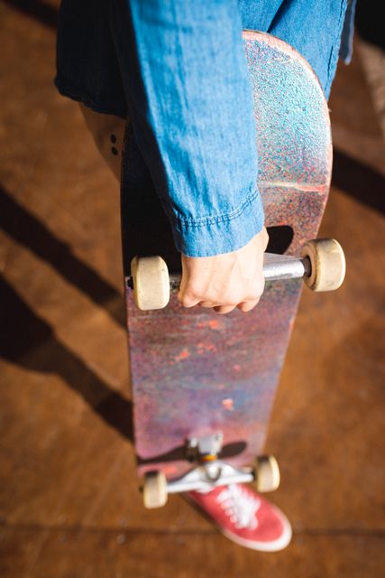 Caucasian man holding skateboard in skatepark on sunny day. Ideal for use in articles or advertisements related to skateboarding, youth culture, outdoor activities, and lifestyle. Suitable for promoting skateboard shops, sportswear brands, and recreational events.