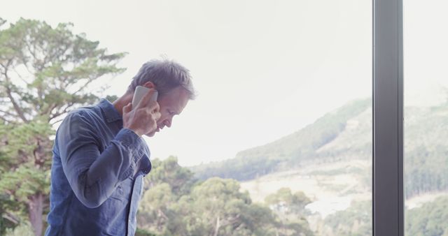 Man Holding Smartphone Near Large Window Overlooking Scenic Outdoor View - Download Free Stock Images Pikwizard.com