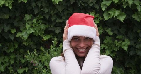 Woman smiling holding santa hat in front of green ivy wall