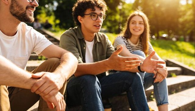 Young adults chatting on park steps sharing coffee and laughter in warm sunlight