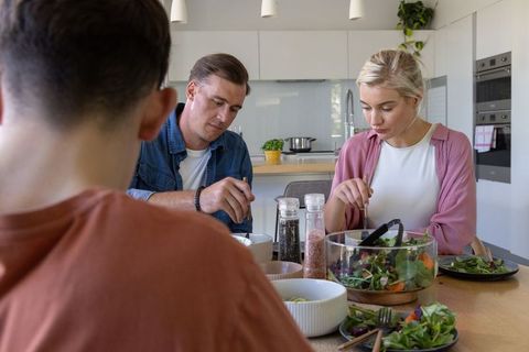 Family sharing healthy salad dinner at modern kitchen table, passing seasonings